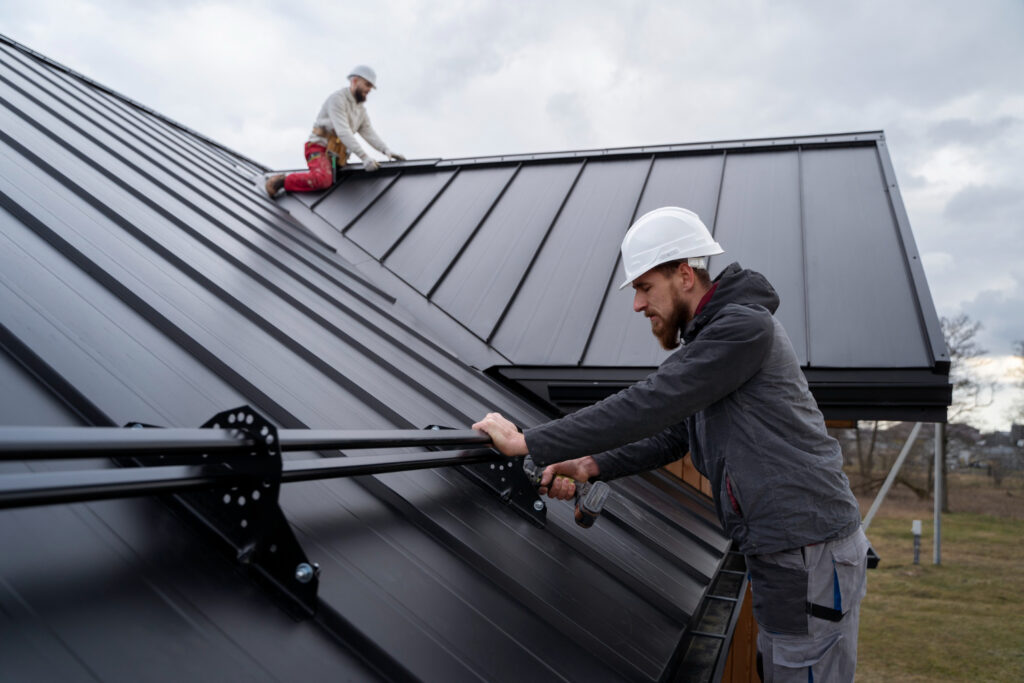 Roofers installing a dark standing seam metal roof on a pitched roof in Austin, TX