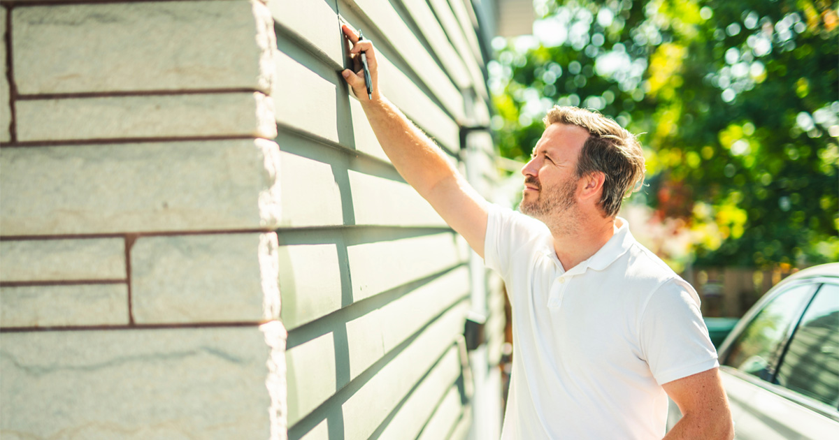 Homeowner inspecting exterior siding for cracks and moisture damage