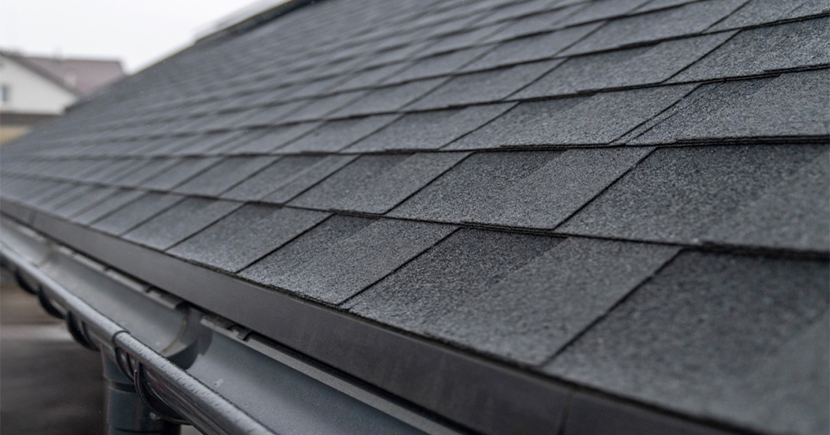 Close-up of dark asphalt shingles and a gutter edge on a residential roof