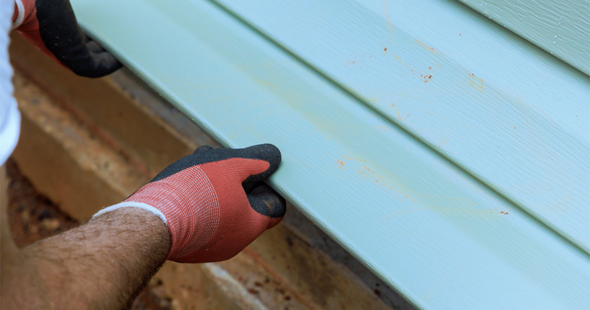 Installer fitting a new light blue vinyl siding panel on an Austin, TX home