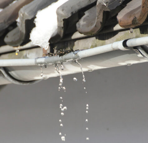 Water dripping from a clogged gutter under a tile roof, a sign of roof drainage problems