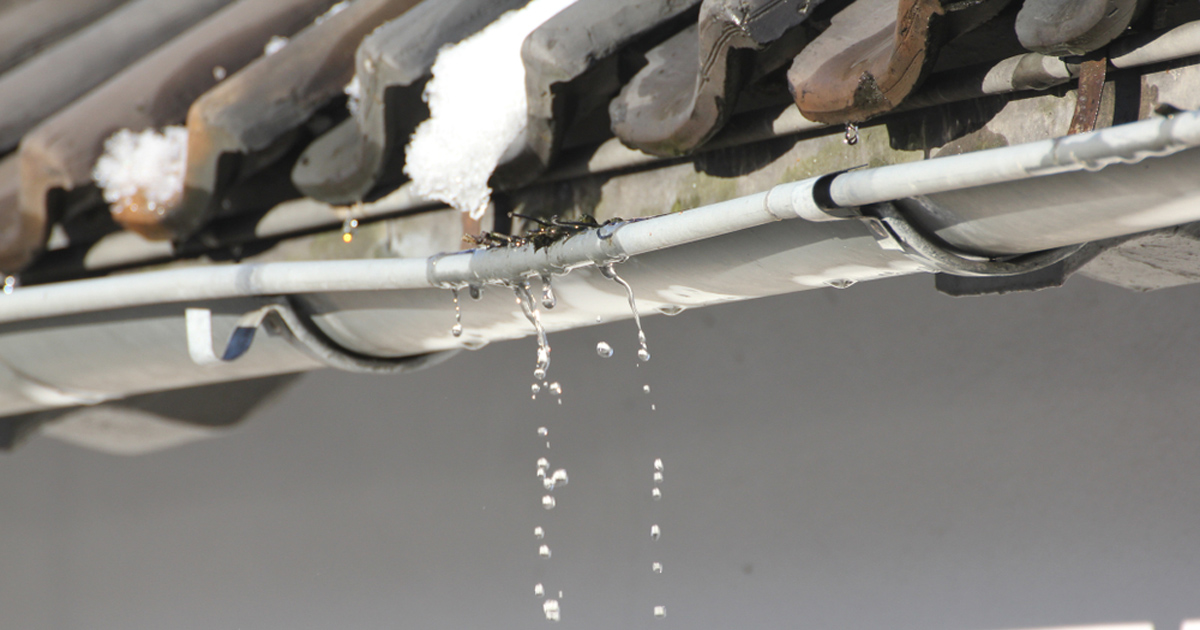 Water dripping from a clogged gutter under a tile roof, a sign of roof drainage problems