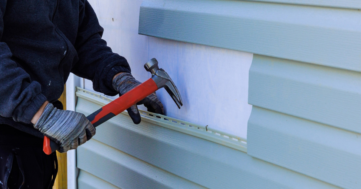 Installer hammering a new light blue siding panel into place during a siding repair in Austin, TX
